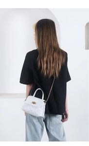 Close-up of white quilted crossbody bag with gold chain strap worn by a model