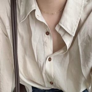 Detail shot of minimalist gold bead chain necklace worn on a cream linen shirt