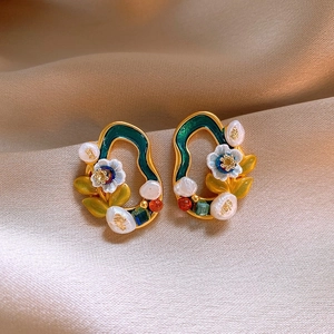 Detailed close-up of vintage enamel pearl earrings with floral motifs on champagne silk fabric