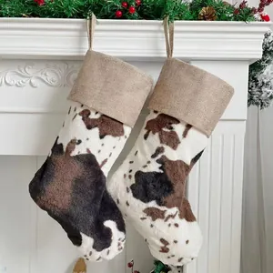 Pair of cow print plush Christmas stockings hanging on fireplace with rustic linen cuffs