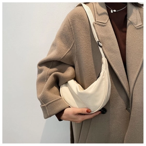 Minimalist beige dumpling-shaped nylon crossbody bag worn over a brown wool winter coat