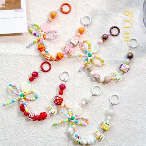 Close-up of colorful beaded phone charms with bows and 'm' letters on a textured background