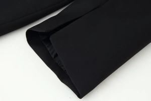 Detail of slit cuff design on black long-sleeved dress with smooth suit fabric texture