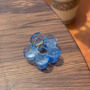 Détail d'une pince à cheveux fleur bleue translucide sur une surface en bois foncé