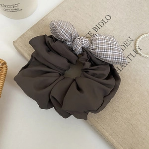Detail of a dark brown fabric hair scrunchie with a black and white grid bow tie decoration