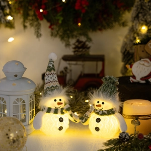 Close-up of glowing Christmas snowman plush with green knit hat and warm LED lights