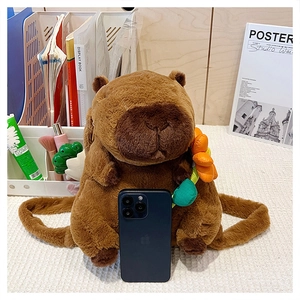 Cute brown capybara plush backpack with flower accessories on a desk with a phone