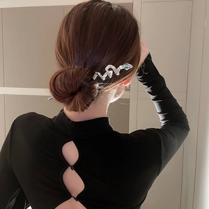 Detailed view of a silver snake-shaped hair pin with green crystal on a low bun hairstyle