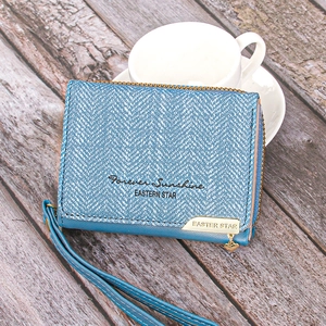 Detail of blue herringbone fabric wallet with heart pendant and leather trim on wooden table