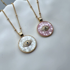 Close-up of gold evil eye pendants with white and pink shell inlay and blue zircon stones