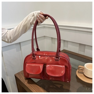 Dettaglio borsa a spalla in pelle verniciata rossa con tasche su tavolo di vetro