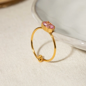 Detail shot of an adjustable 18k gold-plated ring with a pink oval zircon on a ceramic plate