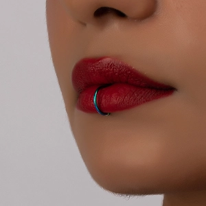 Close-up of rainbow gradient metal lip ring on model with dark red lipstick