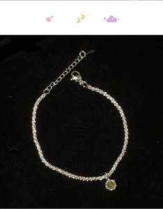 Detail of silver chain bracelet with a round light green gemstone pendant and lobster clasp