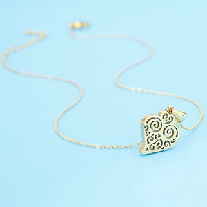 Detail shot of a golden heart necklace with hollow swirl patterns on a blue background