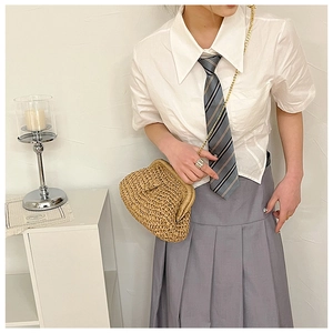 Brown woven straw dumpling bag with gold chain strap held by model in school uniform