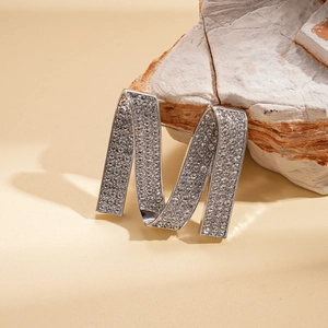 Close-up of a silver letter M brooch with rhinestones resting on a textured stone