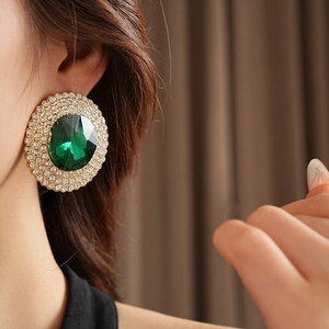 Close-up of emerald green crystal earring with sparkling diamond halo on model