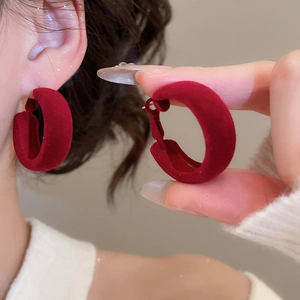 Détail de boucles d'oreilles créoles C rouges avec texture veloutée pour un style hivernal