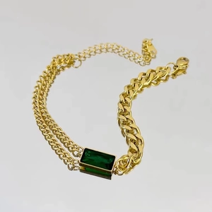 Detail von goldener Titan-Armband mit smaragdgrünem Stein und asymmetrischen Panzerkettengliedern