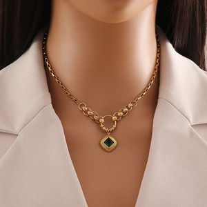 Close-up of emerald green square pendant on golden stainless steel chain worn by model