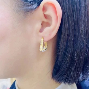Detail of 18K gold-plated U-shaped earrings with small white pearls on a female model
