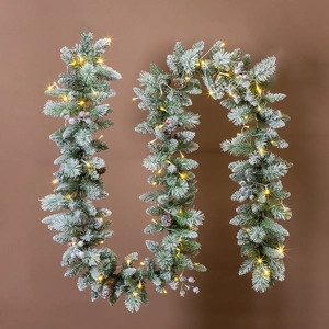 Detail of flocked Christmas garland with pine cones, purple berries and warm LED lights