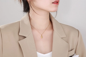 Gros plan d'un collier avec pendentif ovale doré porté sur une veste de tailleur beige