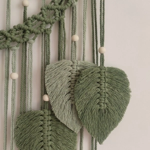 Close-up of bohemian woven wall hanging with green cotton leaf shapes and wooden beads