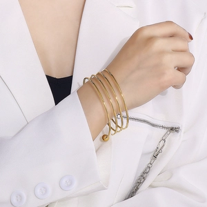 Close-up of a layered gold spiral metal bracelet worn by a model in a white blazer