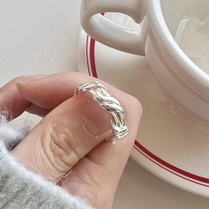 Detail shot of a minimalist silver twisted rope ring worn on finger with a white cup background