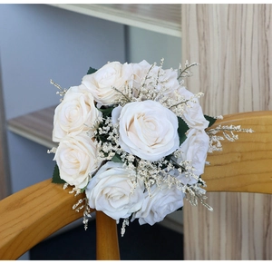 Detail of cream white silk rose bouquet leaning on a wooden chair for wedding decor