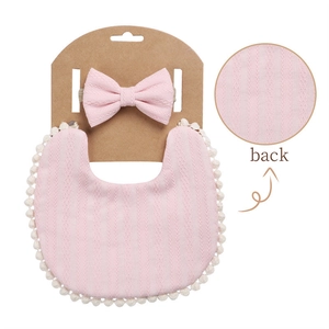 Detailed view of pink knitted baby bib and matching bow headband with soft pom-pom trim