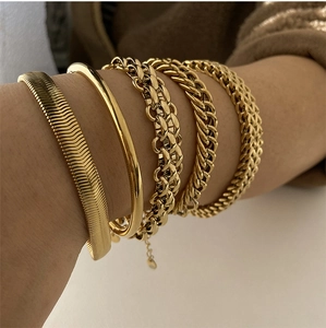 Detailed view of layered gold-plated stainless steel snake and curb chain bracelets on wrist