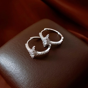 Macro shot of silver zircon star hoop earrings on brown leather and red satin