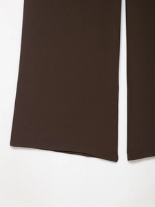 Detail of dark brown wide-leg trousers showing hem stitching and textured crepe fabric
