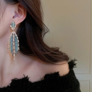 Elegant long gold fringe earrings with teal and clear crystals worn by a fashion model