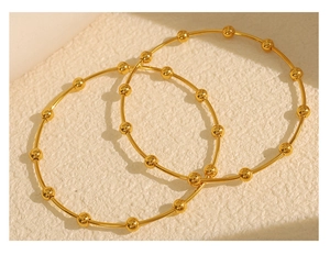 Close-up of minimalist gold beaded bangle bracelets with polished metallic finish