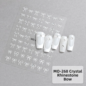 Close-up of 5D white bow nail art stickers with sparkling rhinestones on textured gray background