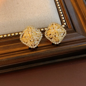 Detailed close-up of gold square earrings with clustered zircon on textured fabric