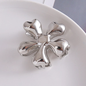Close-up of a glossy silver flower claw clip made of polished metal on a ceramic plate