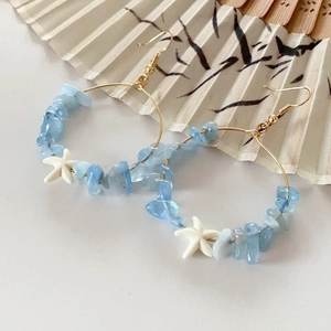 Close-up of gold hoop earrings with light blue crystals and white starfish charms