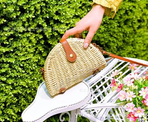 Detail of a semi-circular straw crossbody bag with dark brown leather trim on a white chair