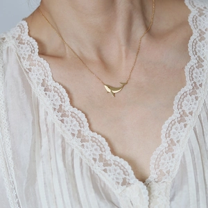 Detailed close-up of a 18K gold plated whale pendant necklace on a white lace collar