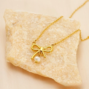 Detailed view of a gold bow pendant with a white pearl on a fine chain necklace