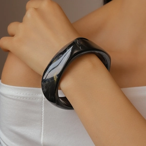 Close-up of wide black resin bangle with marble pattern and golden swirls on a wrist
