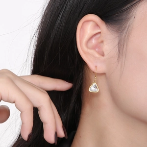 Close-up of model wearing gold triangle crystal drop earrings with hook design