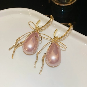 Detail of gold bow earrings with pink teardrop pearl and clear zircon pavé setting