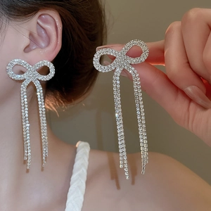 Detail showing sparkling bow earrings with long rhinestone tassels on a silver needle