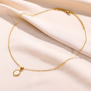 Close-up of gold oval letter K pendant necklace on a premium textured beige fabric